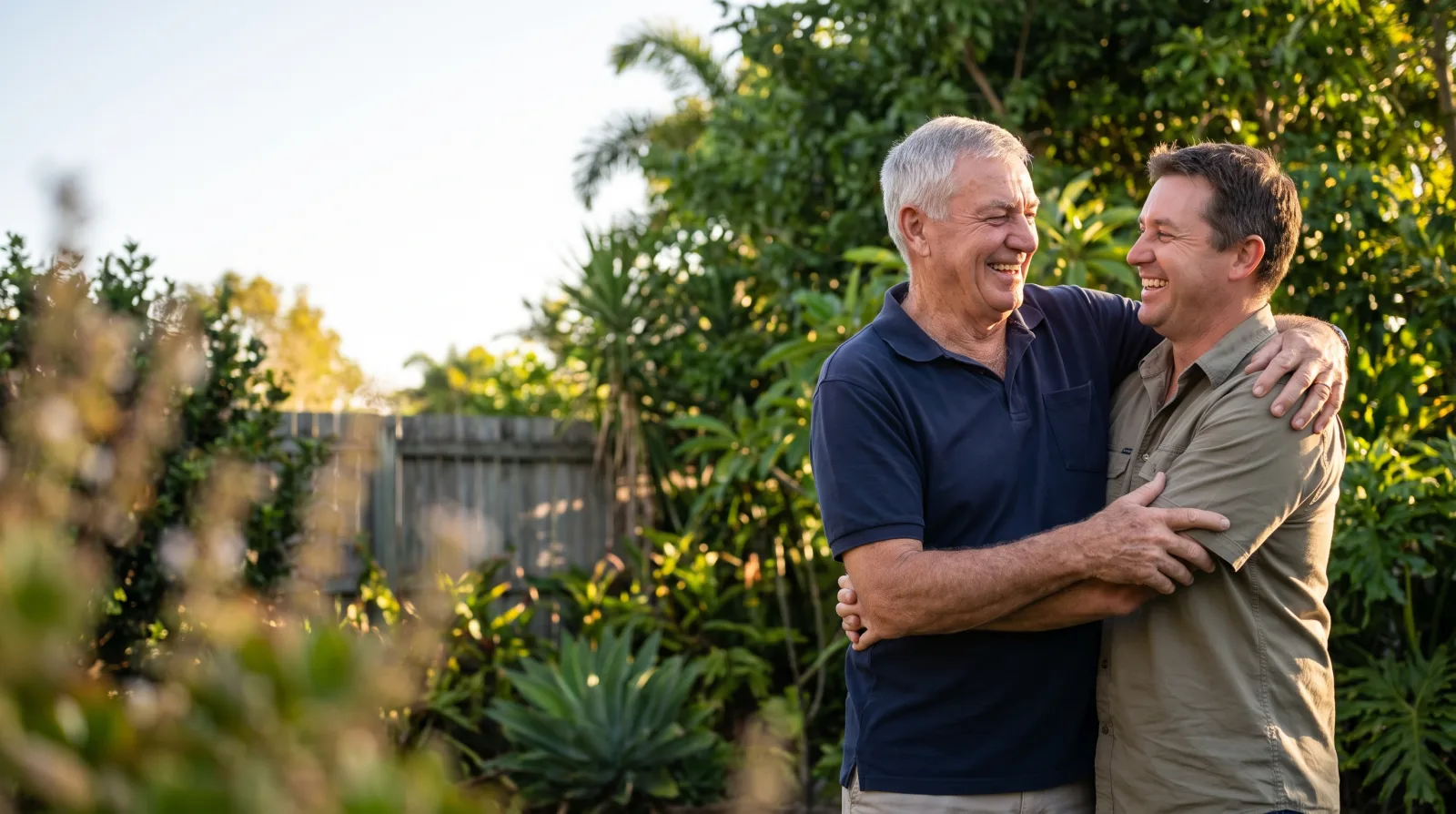 An older father and his adult son laughing together in a sunny Central Queensland backyard on Father's Day
